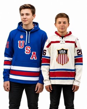 Two boys modeling USA hockey themed apparel, standing side-by-side against a white background. The boy on the left wears a blue hoodie with red and white 'USA' lettering and stripes.