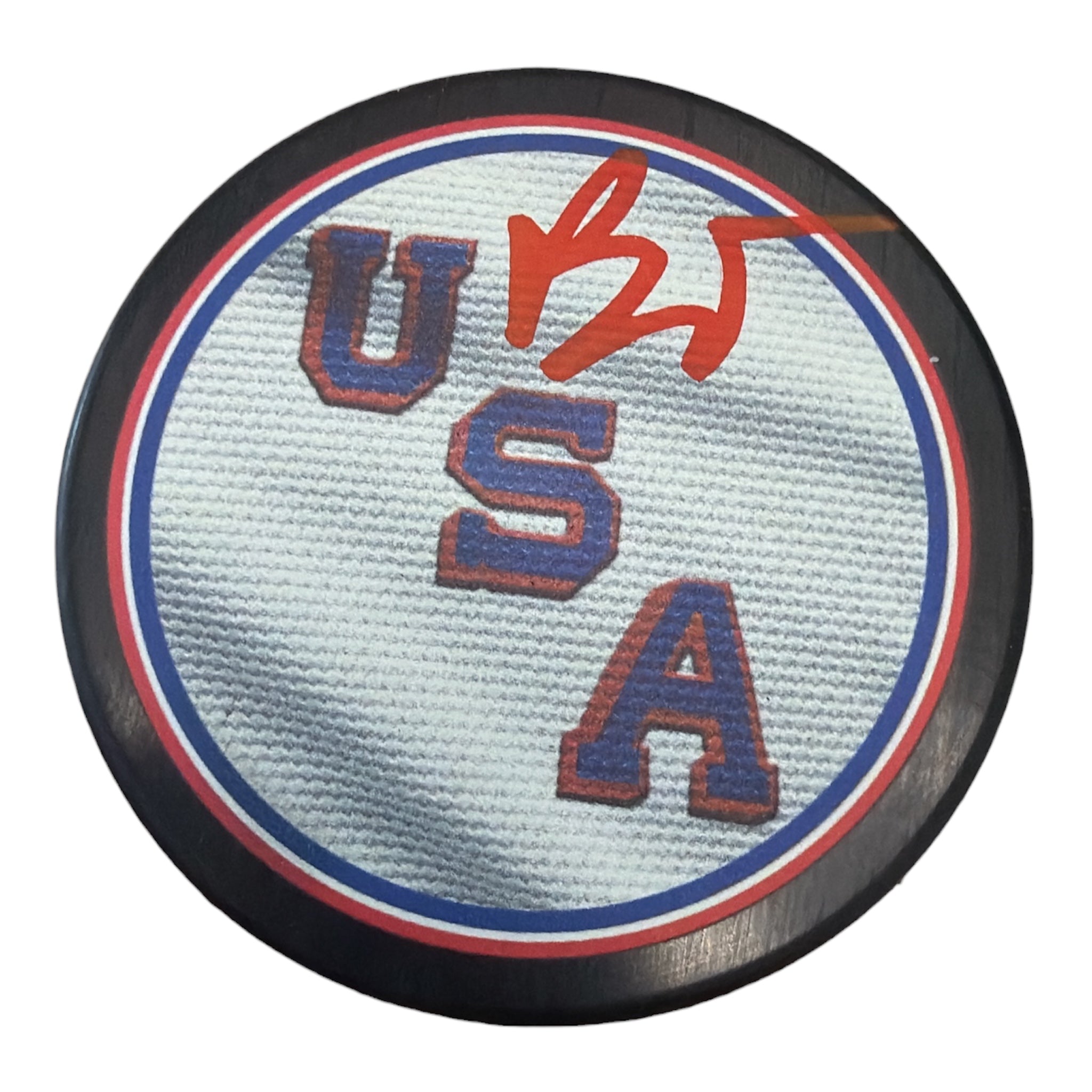 A circular USA hockey puck with a white textured center, blue and red borders, and red embroidered letters spelling USA, with a red autograph on top, shown on a white background.