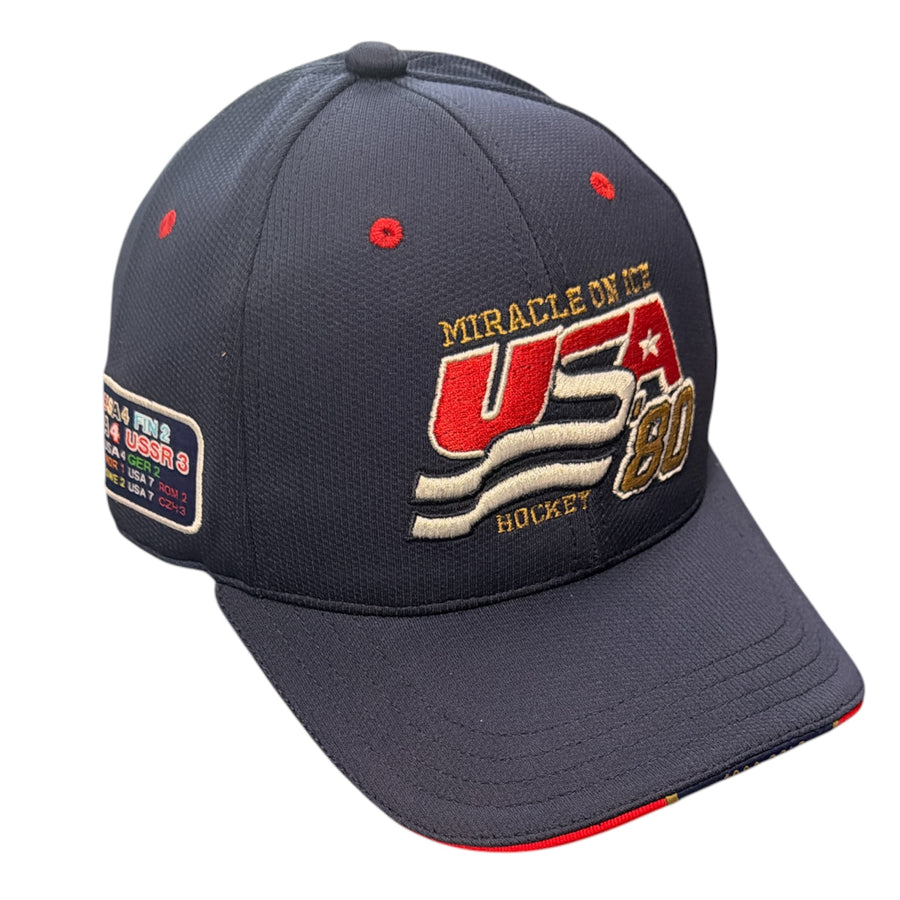 A dark navy blue baseball cap featuring embroidered 'MIRACLE ON IT USA 80 HOCKEY' text on the front panel, with red and gold accents. A rectangular patch is visible on the side.