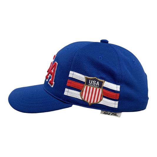 A royal blue baseball cap featuring embroidered USA Hockey branding, including a red, white, and blue shield crest on the side and red embroidered letters on the front, shown against a plain white background.