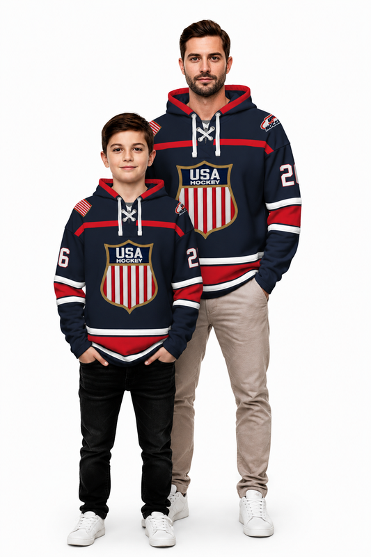 A man and a boy modeling matching USA Hockey hoodies designed like hockey jerseys. The hoodies are navy blue with red and white stripes, featuring a large USA Hockey shield logo on the chest, white drawstrings, and the number 2 on the sleeve.