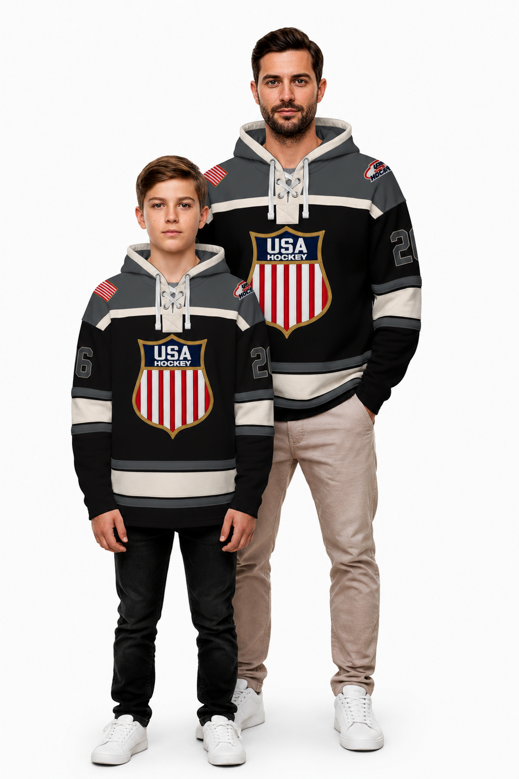 A man and a boy modeling matching black, gray, and white USA Hockey hoodies with red and white shield logos, standing against a plain white studio background.