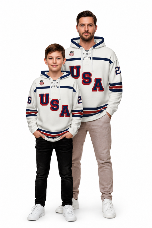 A man and a boy modeling matching white USA hockey-themed hoodies against a plain white background. The hoodies feature 'USA' in red and navy lettering, navy and red striped sleeves, and small shield logos on the chest.